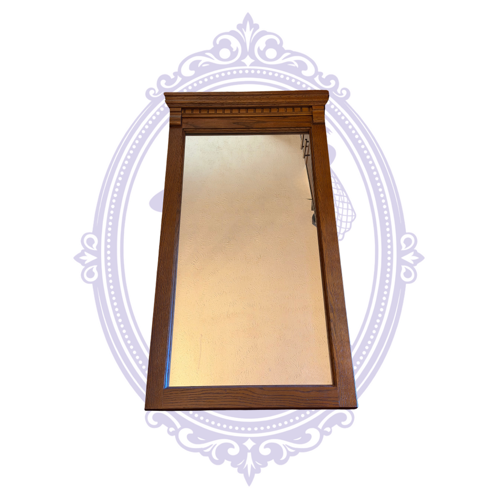 Front view of oak-tone framed rectangular wall mirror on pale lavender decorative backdrop