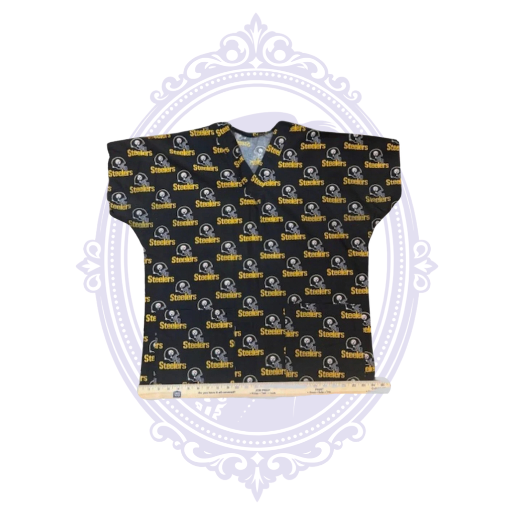 Pittsburgh Steelers helmet print scrub top laid flat with ruler across the bottom hem for width measurement.