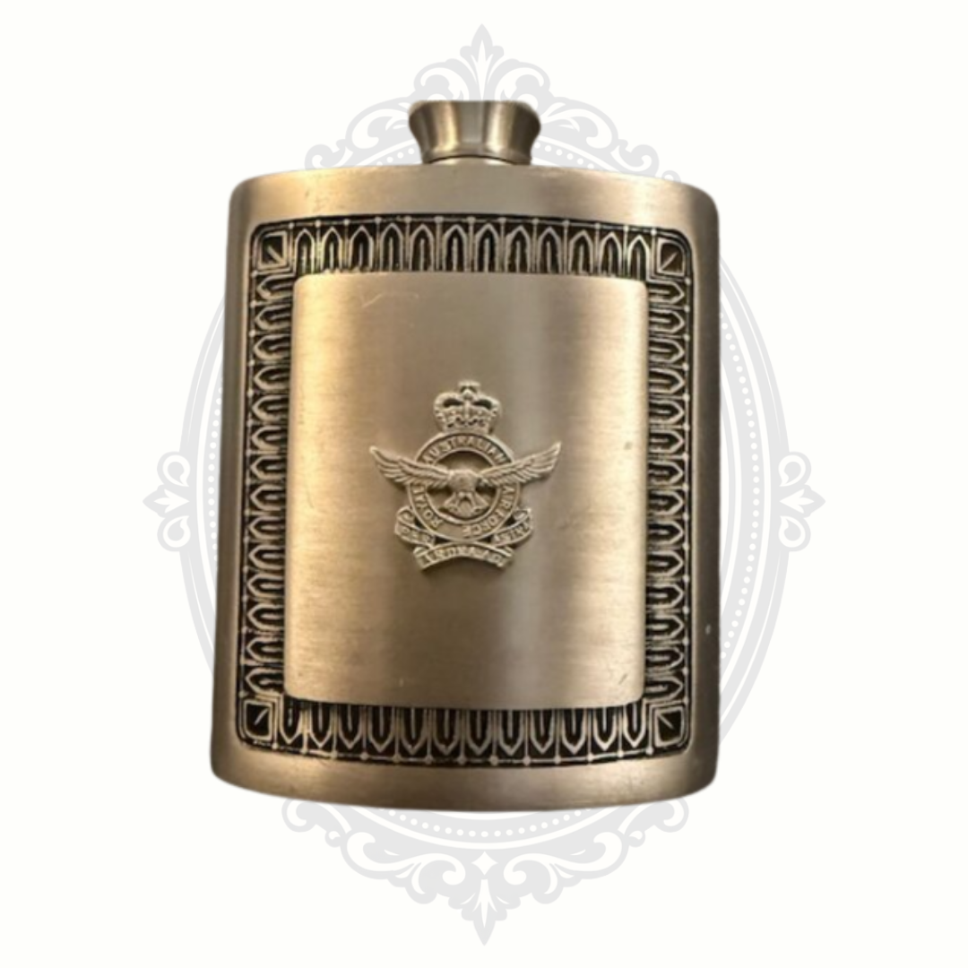 Vintage brass hip flask featuring a raised aviation emblem with wings and crown, framed by an ornate geometric border design