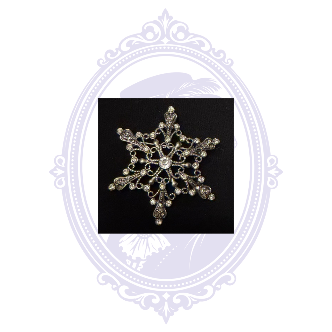 Front view of ornate silver-tone snowflake brooch showing clear rhinestones and large round center stone.