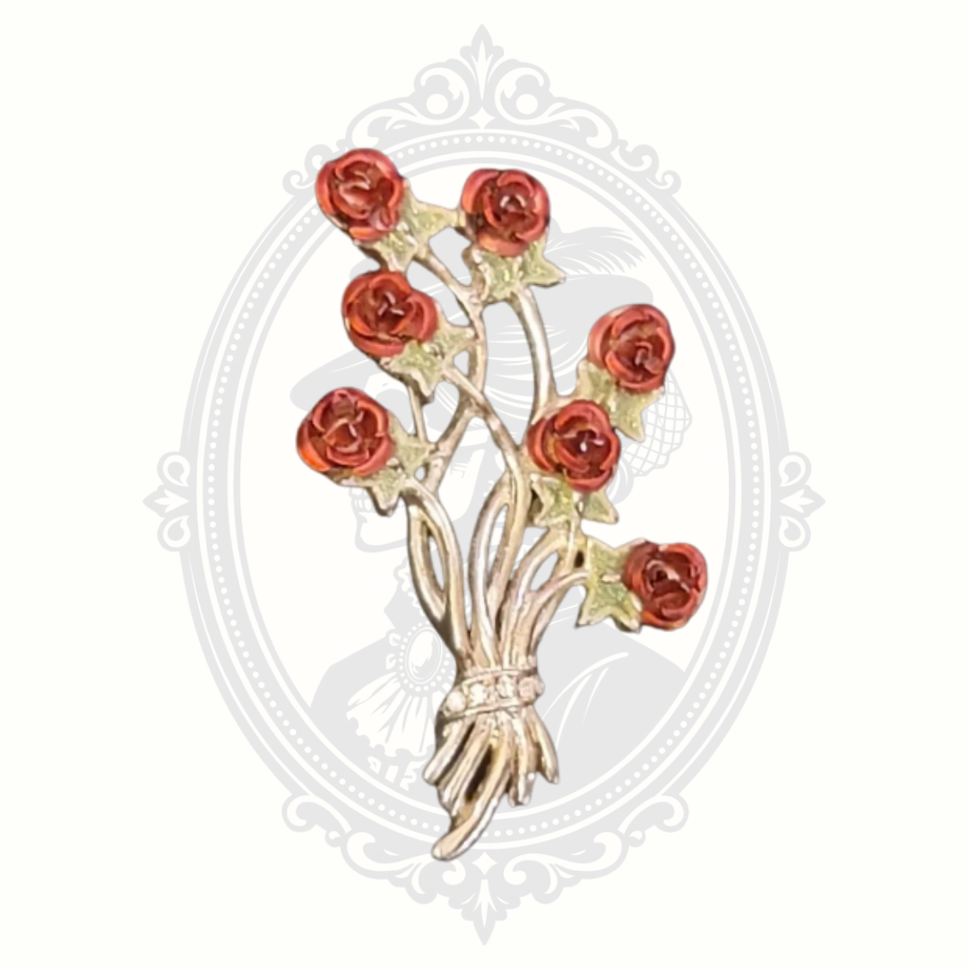 Vintage-style rose bouquet brooch with red enamel flowers and silver-tone stems tied with a rhinestone-accented ribbon.
