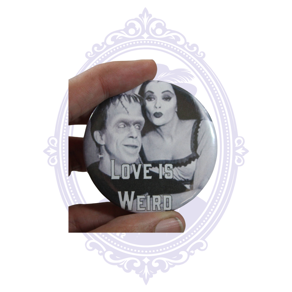 Hand holding 2.25-inch Love Is Weird Munsters pin button showing its size