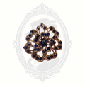 Vintage floral brooch with deep blue rhinestones set in gold-tone metal, featuring intricate openwork detailing and displayed on a soft neutral background with a faint Victorian cameo design.