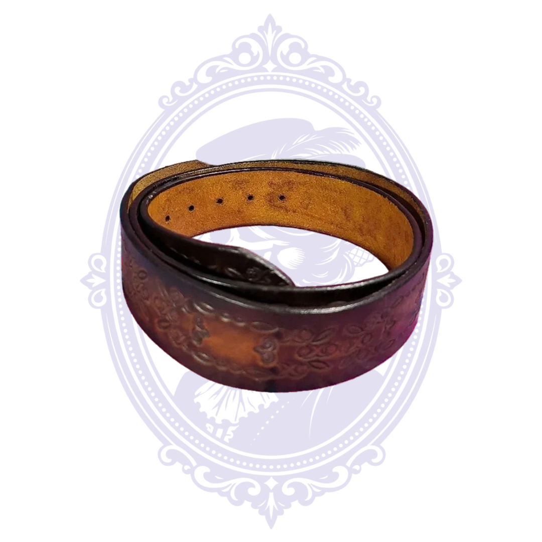 Coiled brown leather belt with embossed floral scrollwork and rectangular panel motifs, showing the tan underside and adjustment holes.