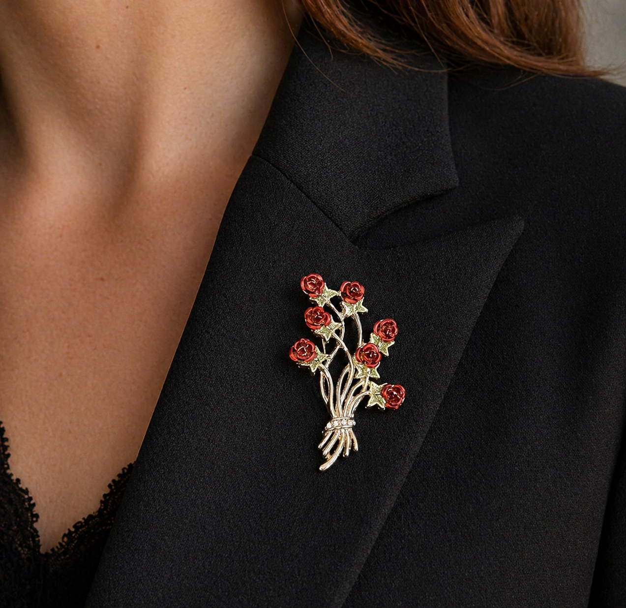 Close-up of a vintage red rose brooch worn on a black blazer lapel, showcasing detailed floral design with clustered roses and silver-tone stems.